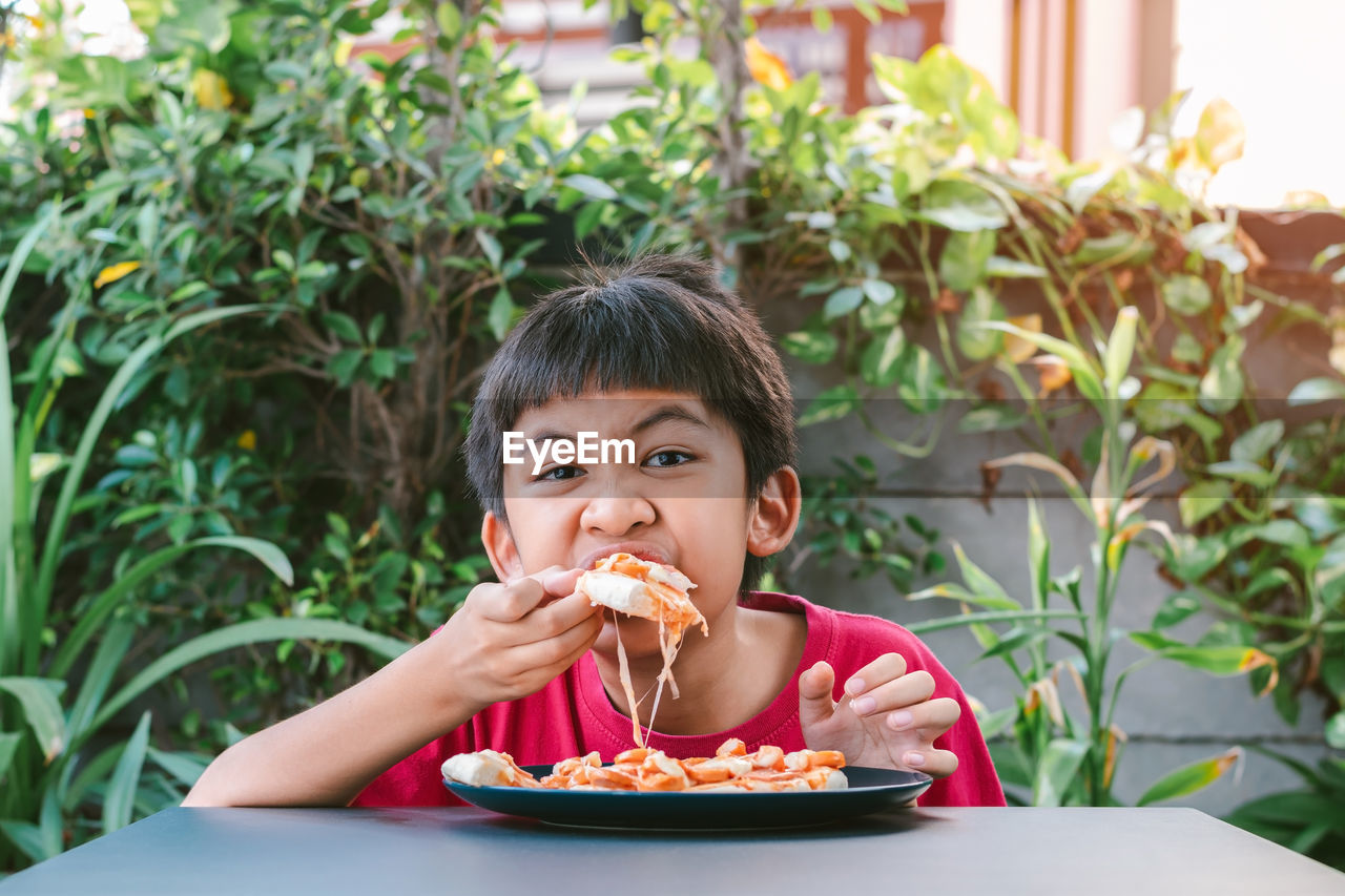 Asian cute boy in red shirt happily sitting eating pizza.