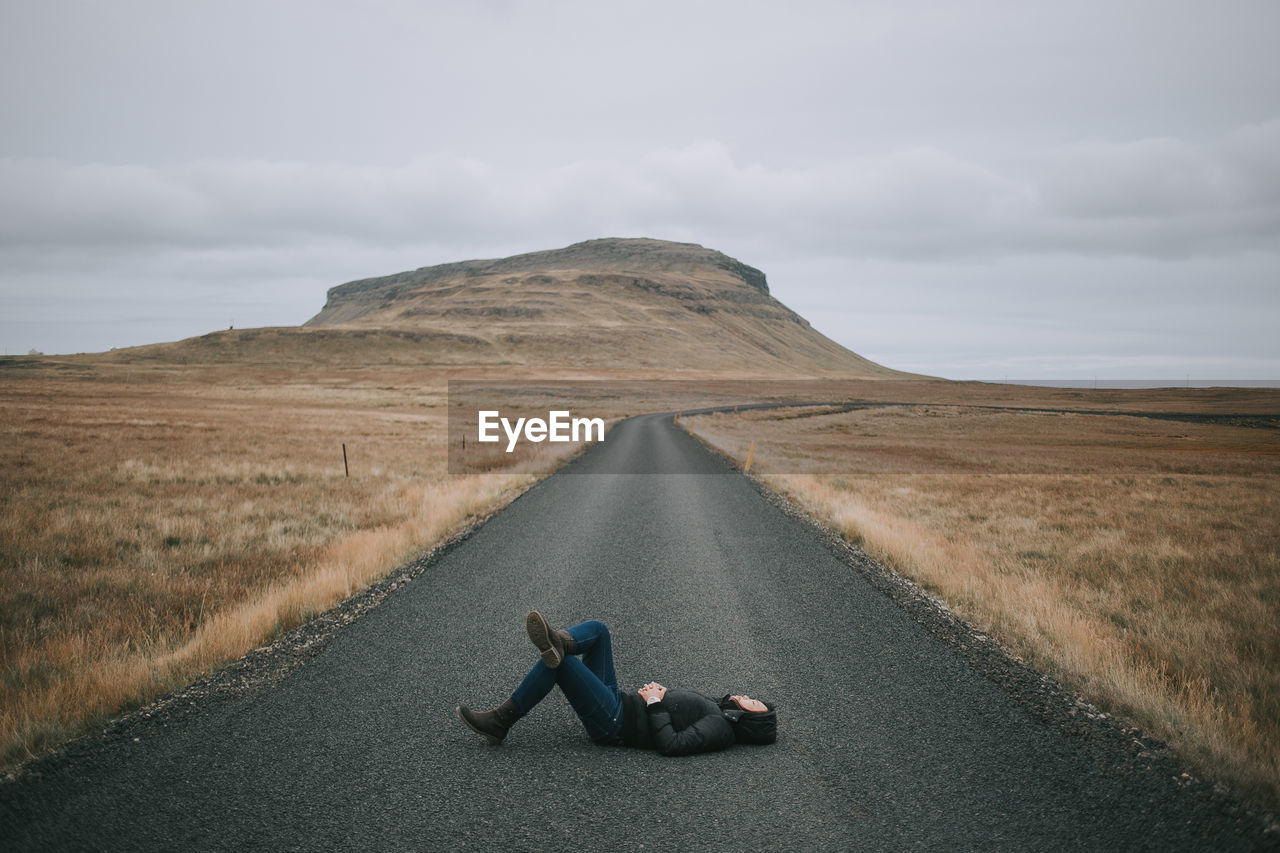 Woman lying on road against sky