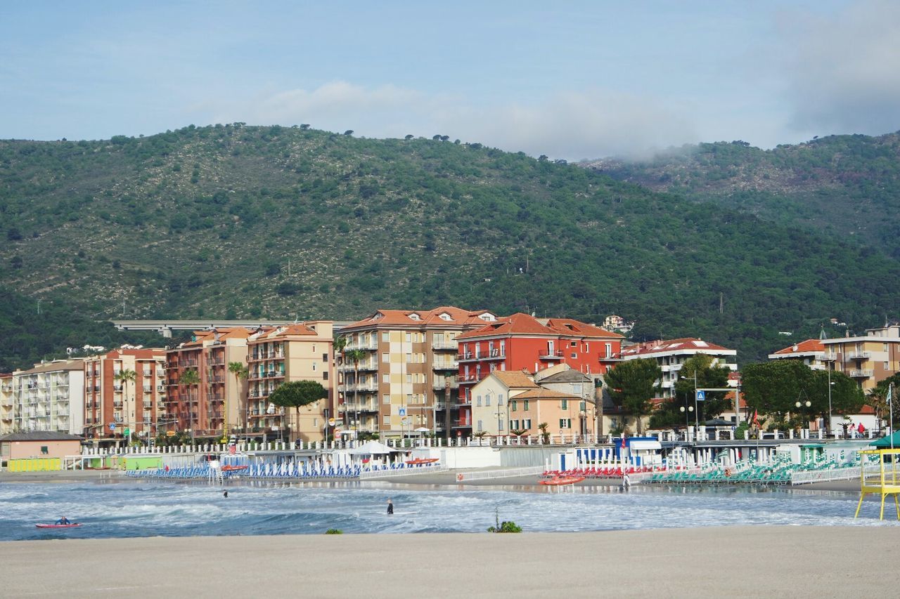 Scenic view of beach in front of buildings and mountains in city