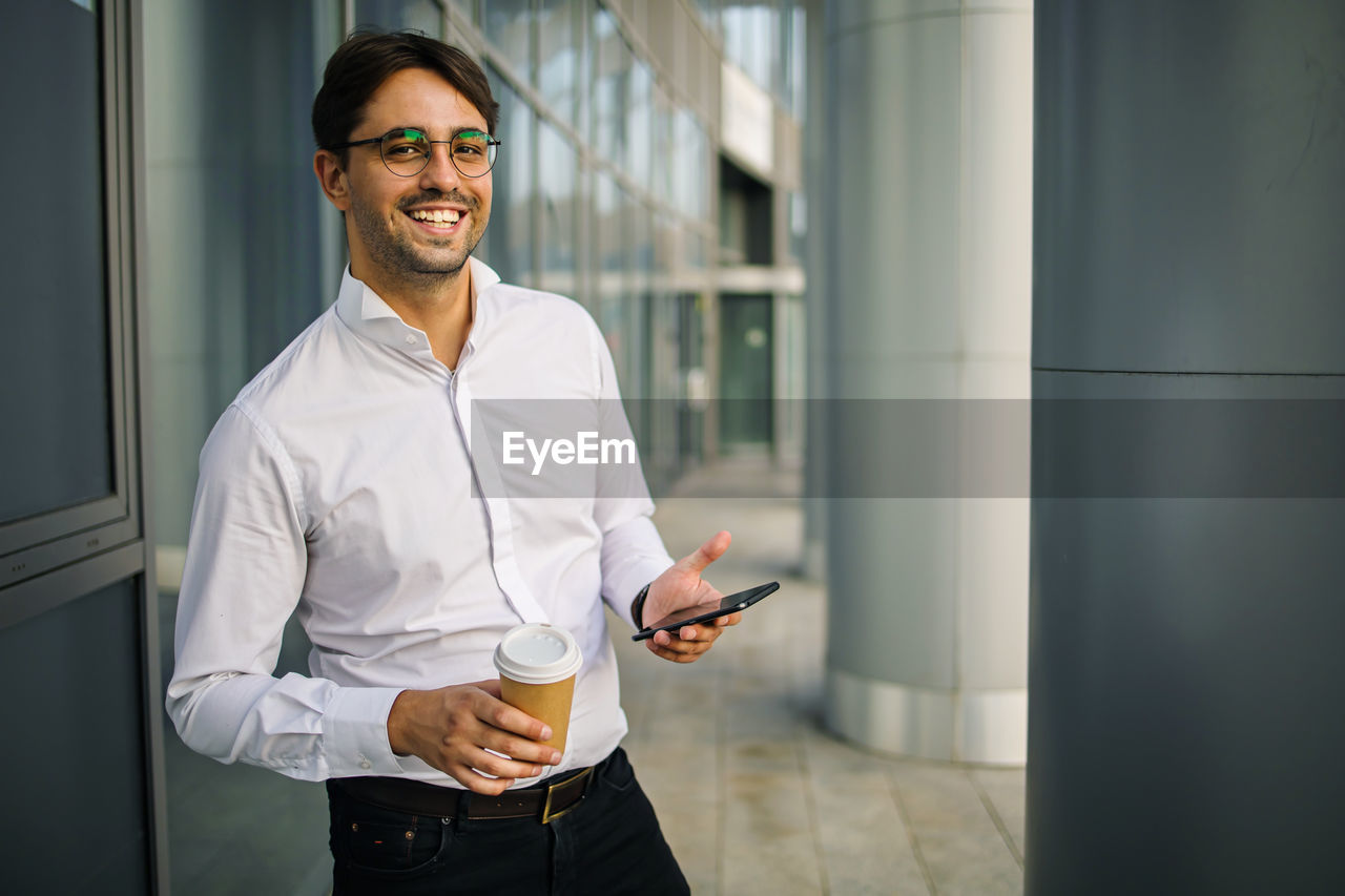 Portrait of young smilling business man standing near office building