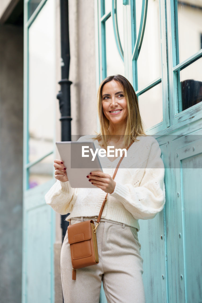 portrait of smiling young woman using mobile phone while standing in office