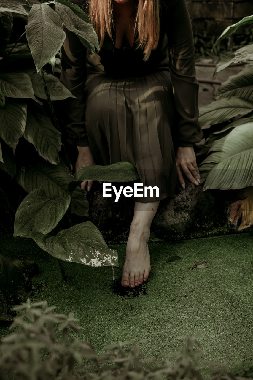 Low section of woman sitting by plants