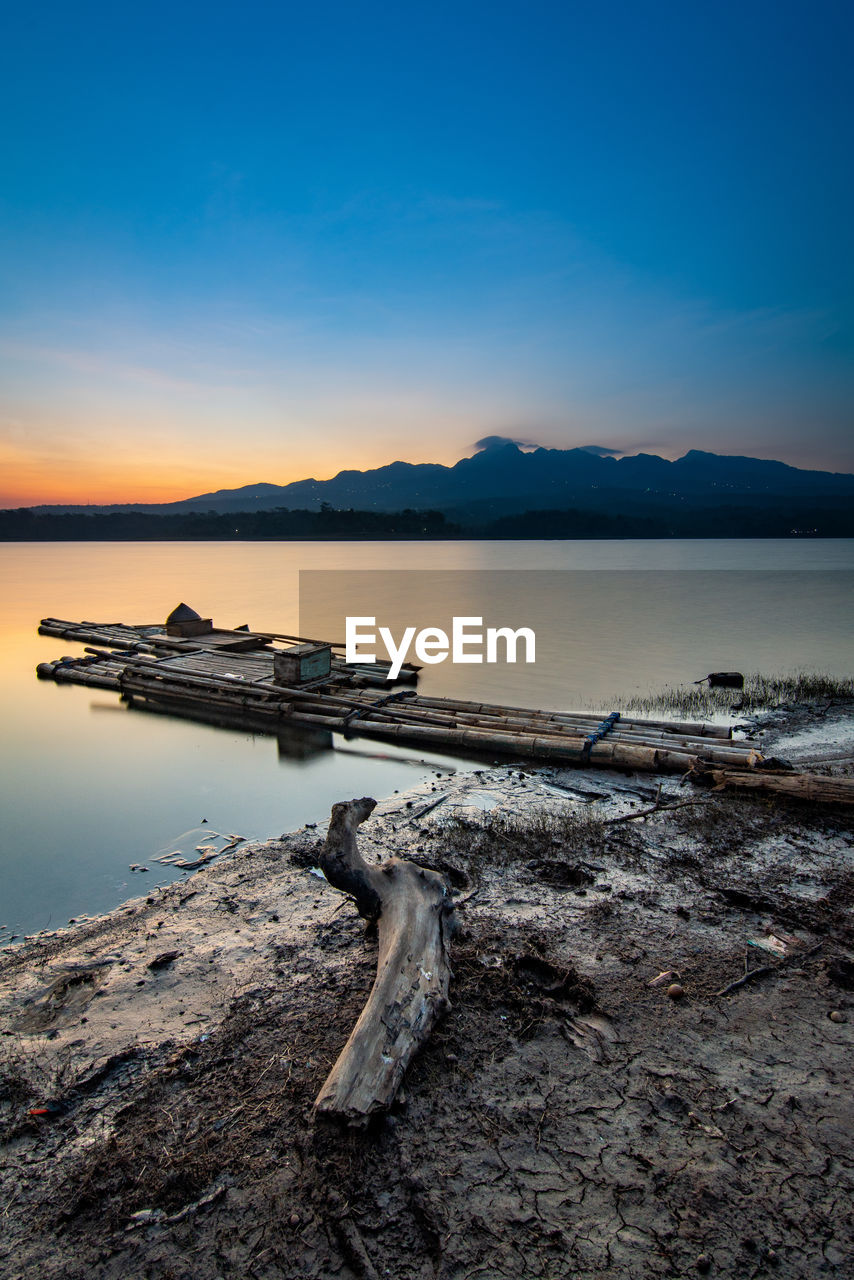 Driftwood on beach against sky during sunset