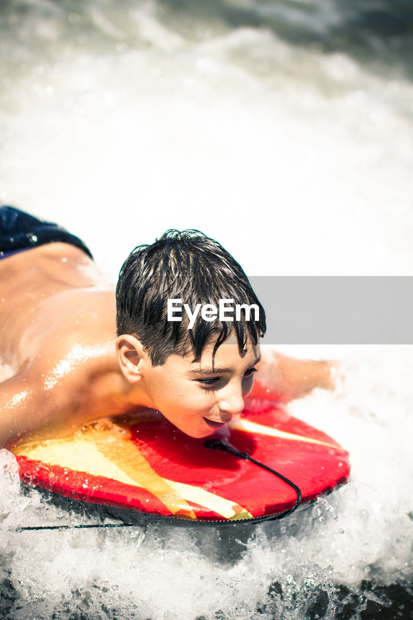 Happy boy surfing in sea during sunny day