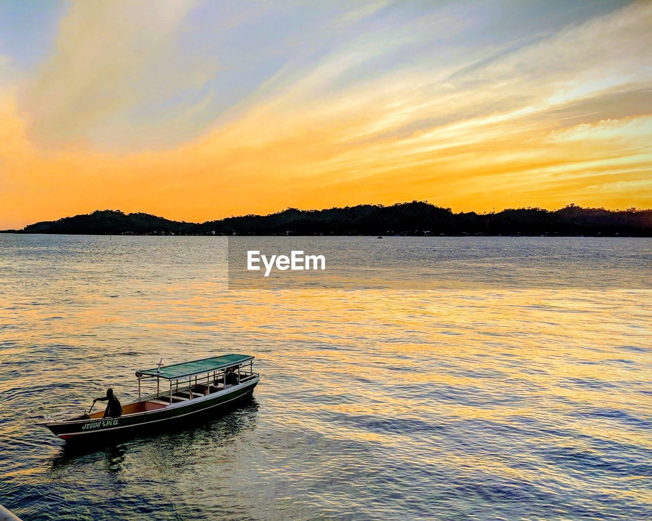 BOAT SAILING IN SEA AGAINST SKY DURING SUNSET