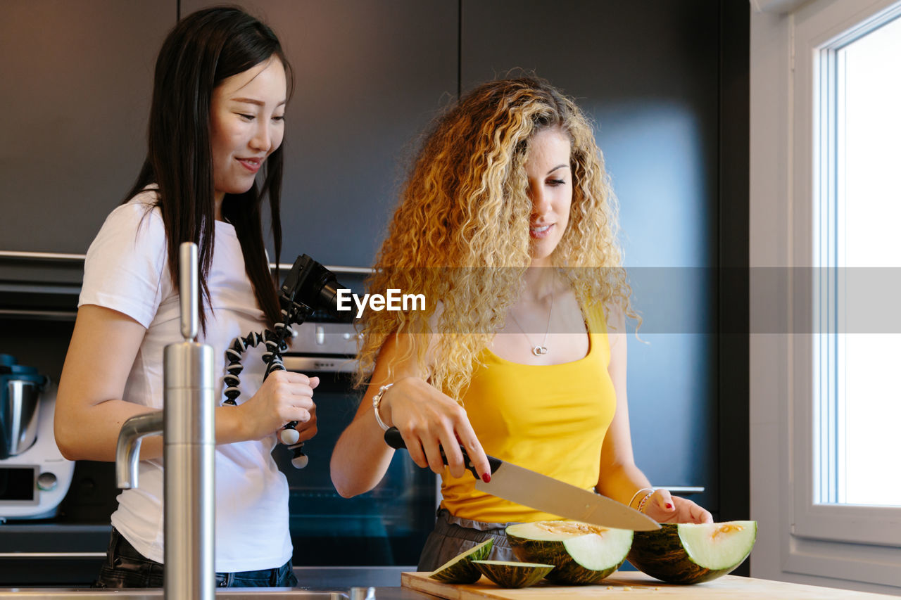 YOUNG WOMAN STANDING BY VEGETABLES AT HOME