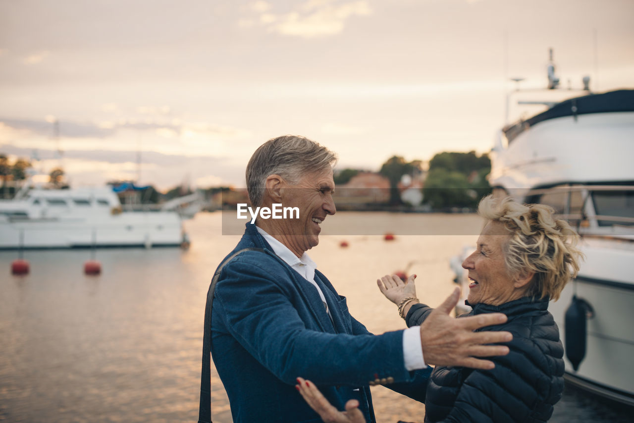 Side view of excited senior woman embracing man at harbor