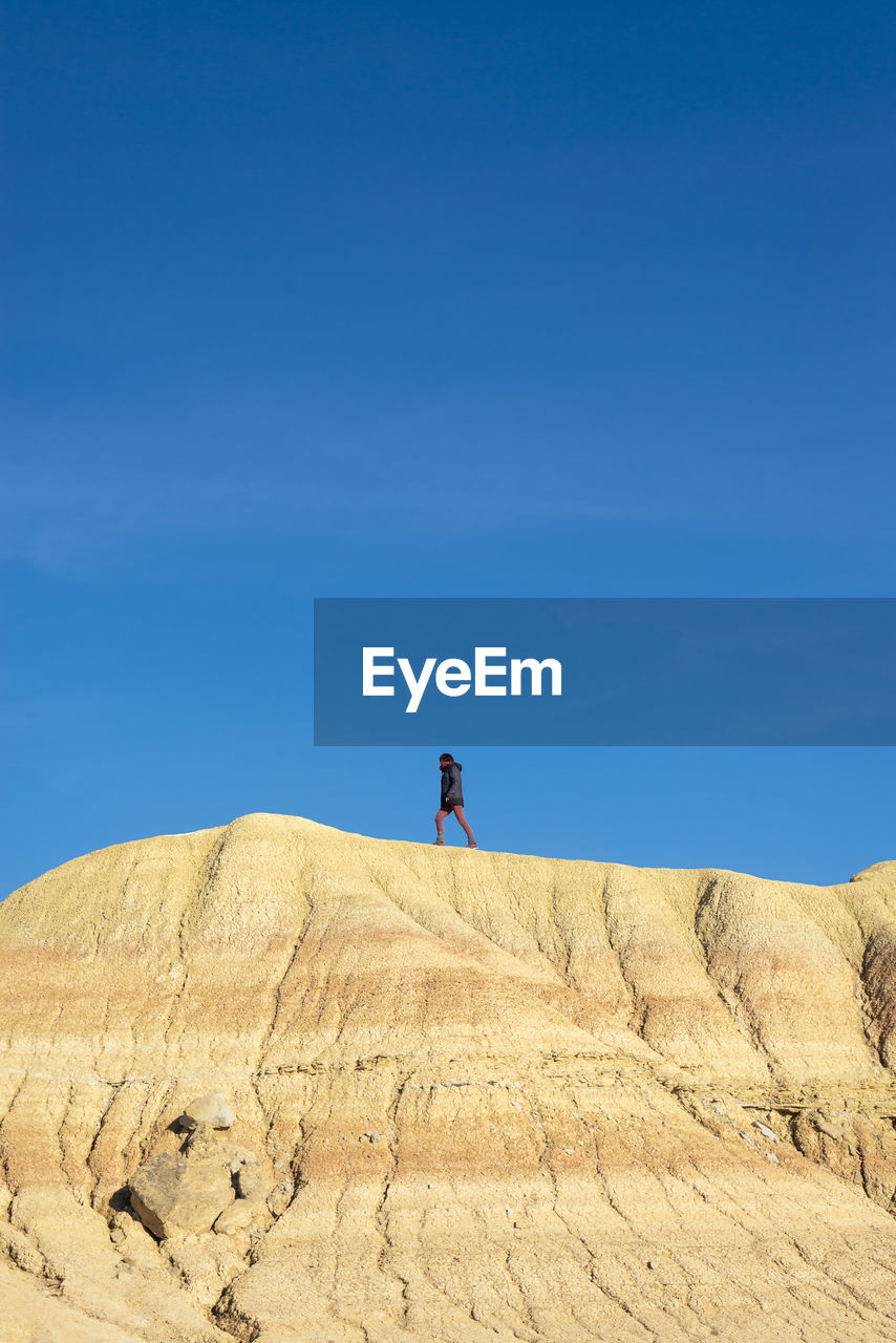 Woman walking on a hill in a desertic landscape against blue sky