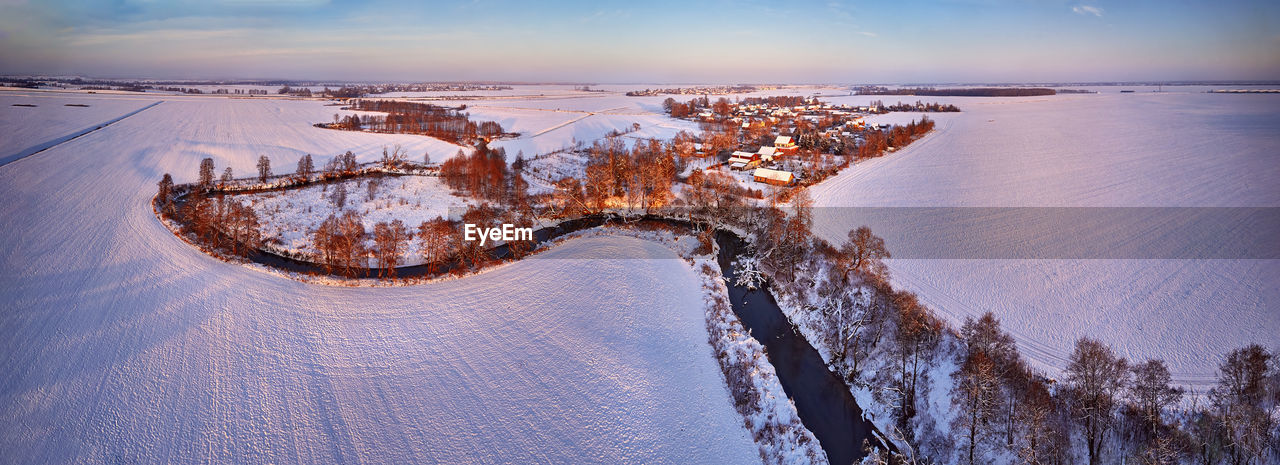 Winter rural panorama. snow covered fields, meadows. river, frozen trees, village in evening light