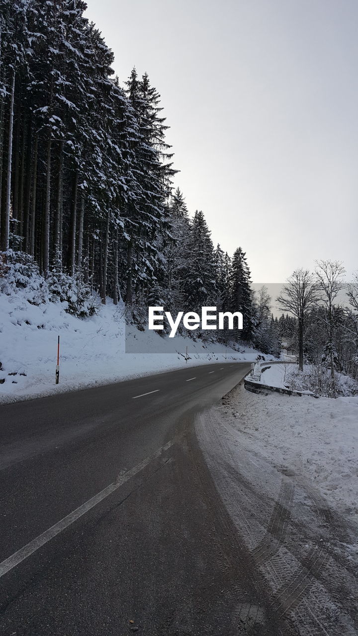 Road amidst trees against clear sky during winter