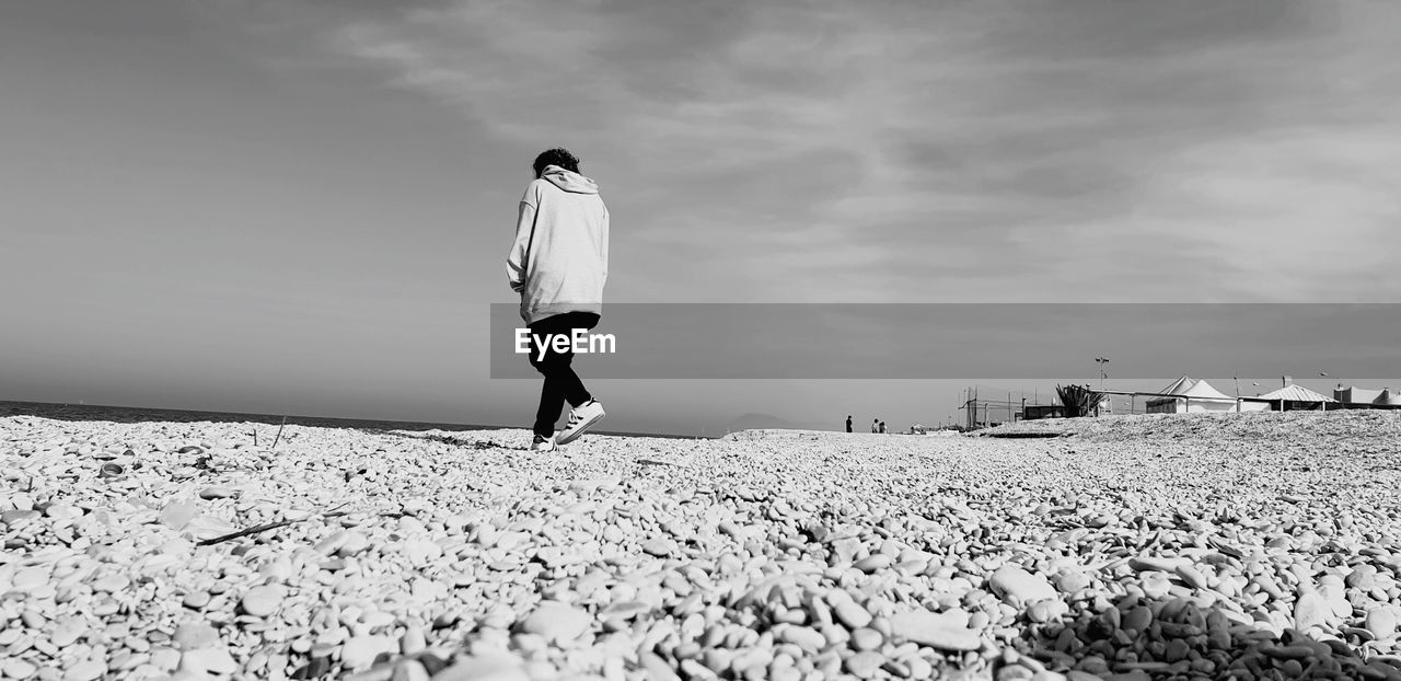 REAR VIEW OF WOMAN STANDING ON PEBBLES ON FIELD