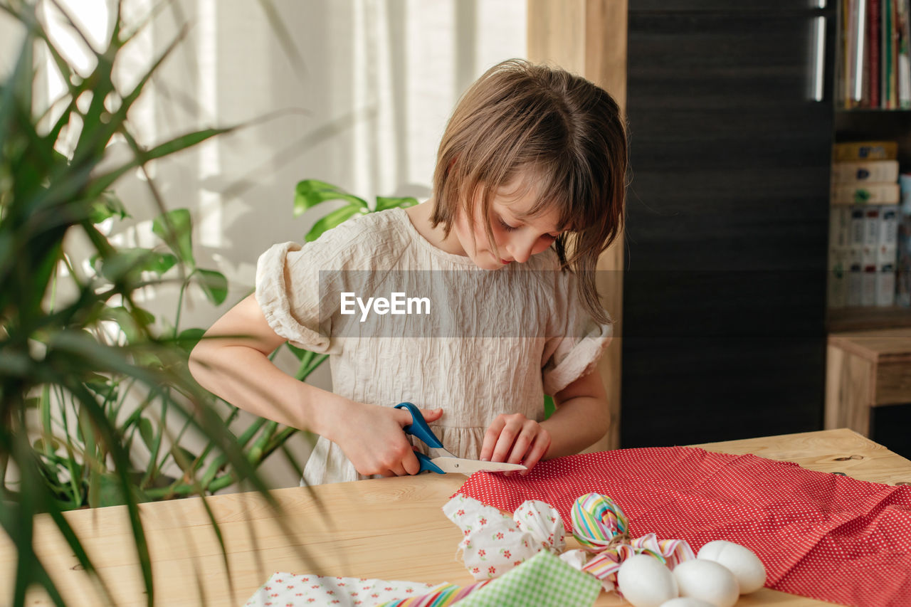 A girl at home prepares fabric for making easter textile eggs in the shape of a hare with ears.