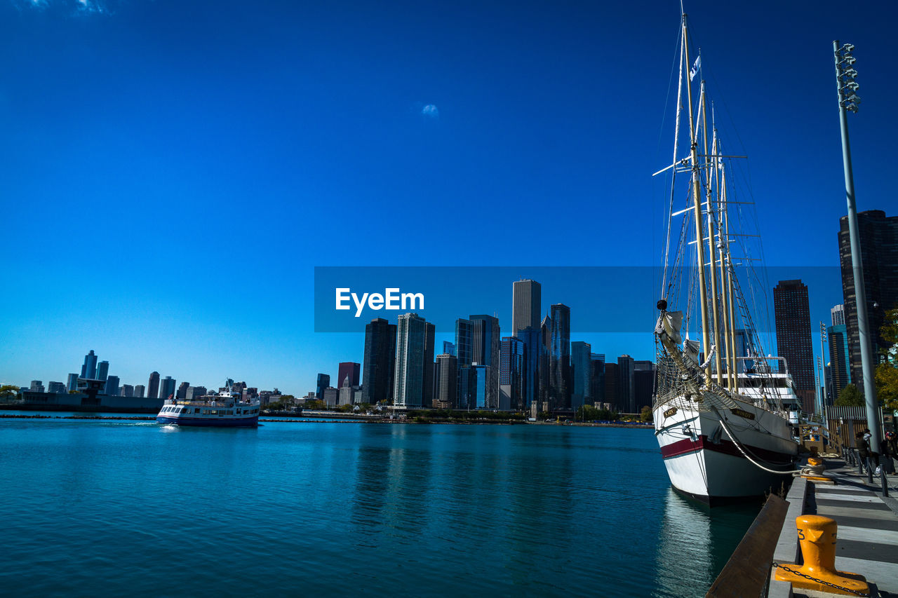 Boats moored in calm sea against clear blue sky