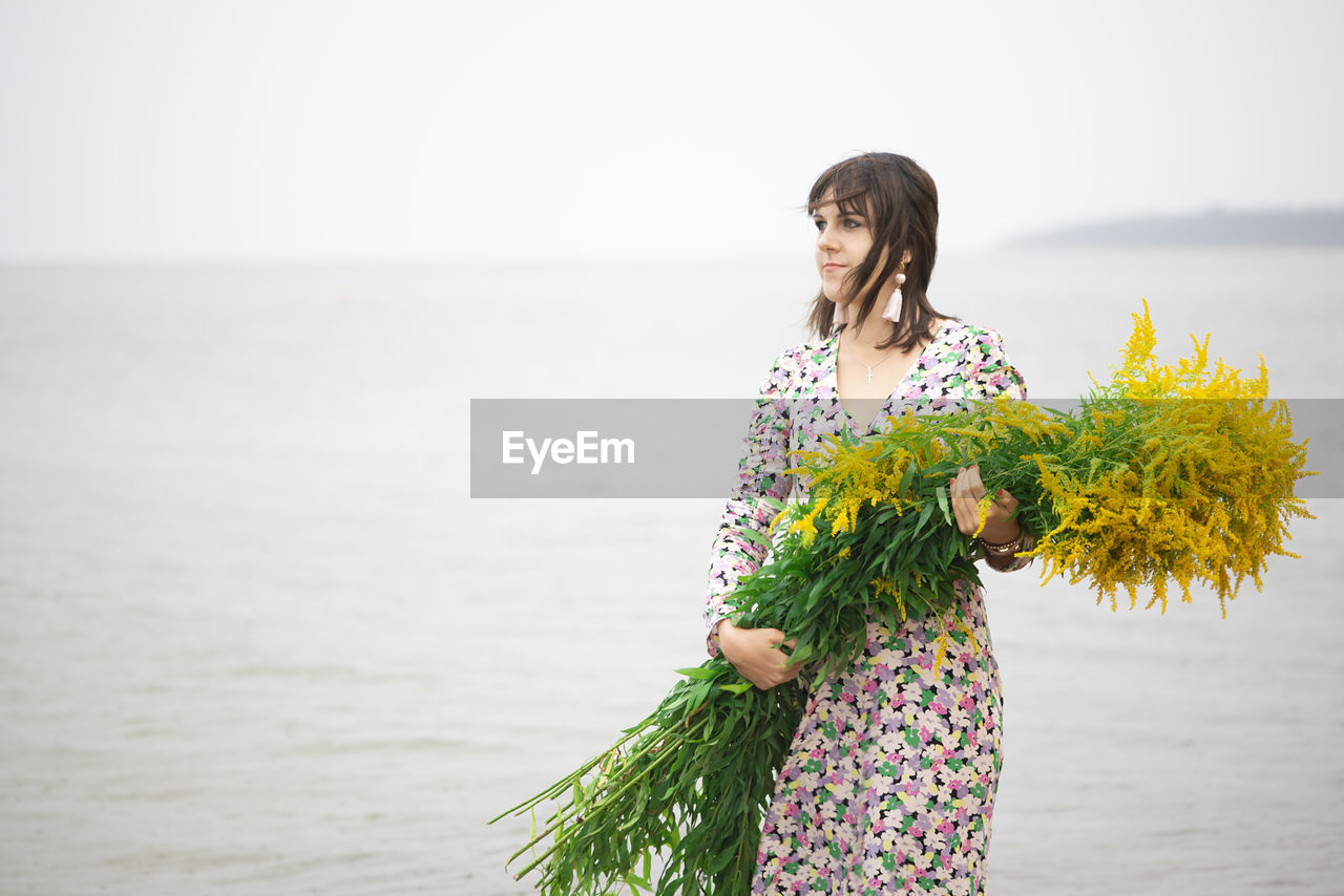 Young beautiful woman with a large bouquet of wild flowers posing on the beach