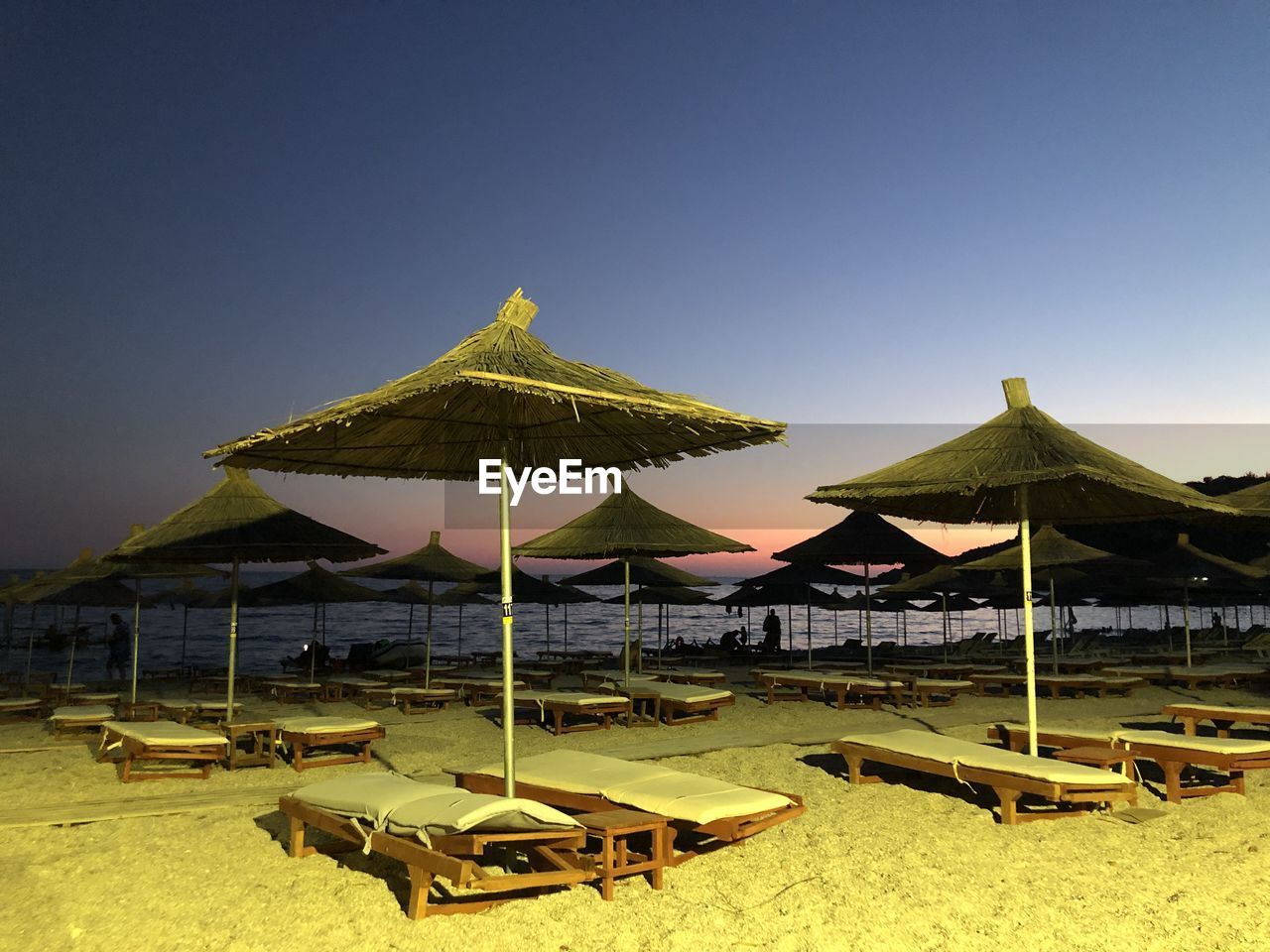 land, sky, parasol, beach, nature, umbrella, sunshade, beach umbrella, sand, chair, thatched roof, shade, tranquility, beauty in nature, travel destinations, water, sea, lounge chair, relaxation, summer, tranquil scene, no people, scenics - nature, roof, vacation, trip, seat, travel, architecture, sunlight, holiday, absence, protection, outdoors, clear sky, idyllic, yellow, sunny, day, tourism, deck chair, security, copy space, blue, environment, hut