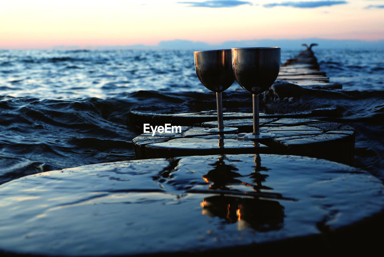 Close-up of beer in sea against sky during sunset