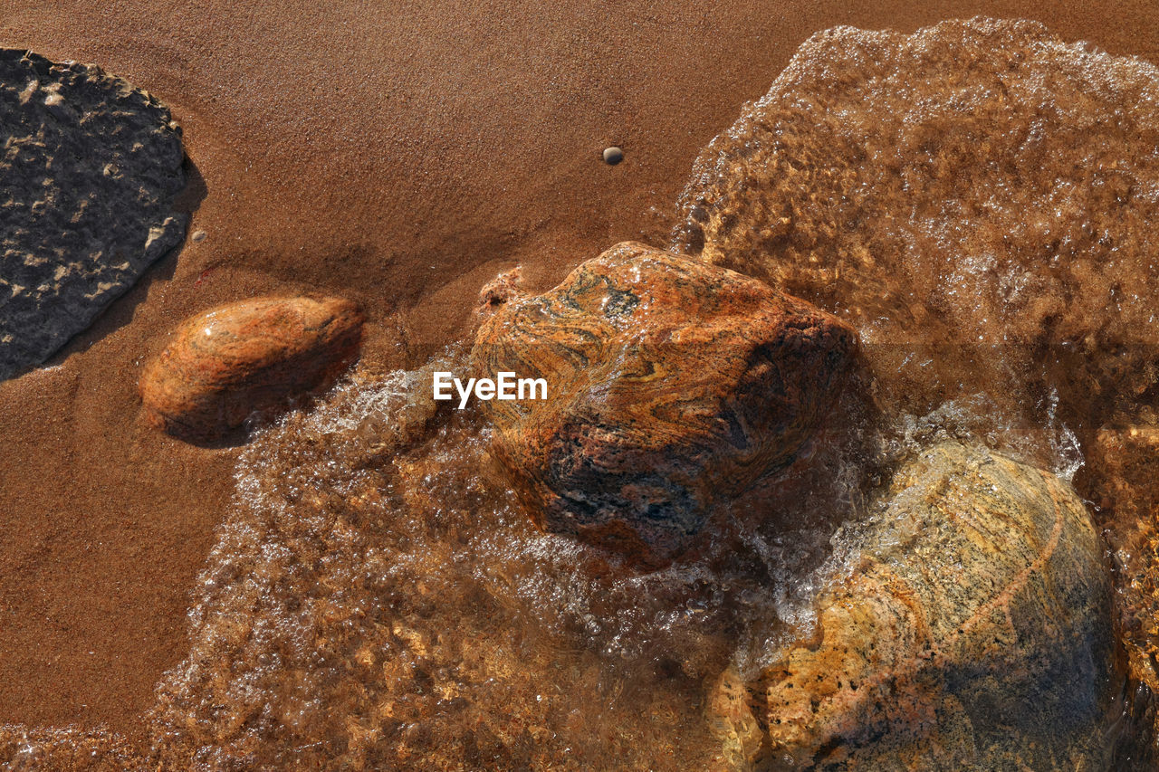 Directly above shot of small pristine waves rolling into beach dotted with colorful rocks boulders