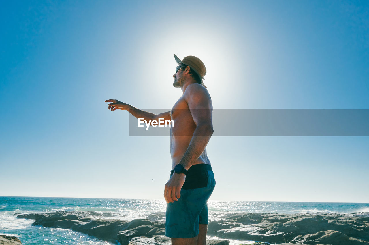 Shirtless young man pointing to the ocean in baja, mexico.