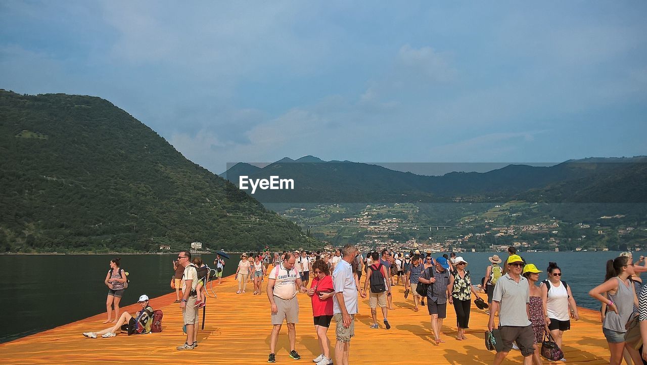 People on wooden pier over lake against sky