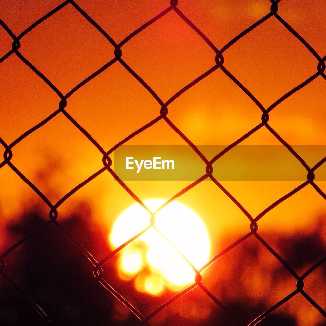 Sun seen through chainlink fence during sunset