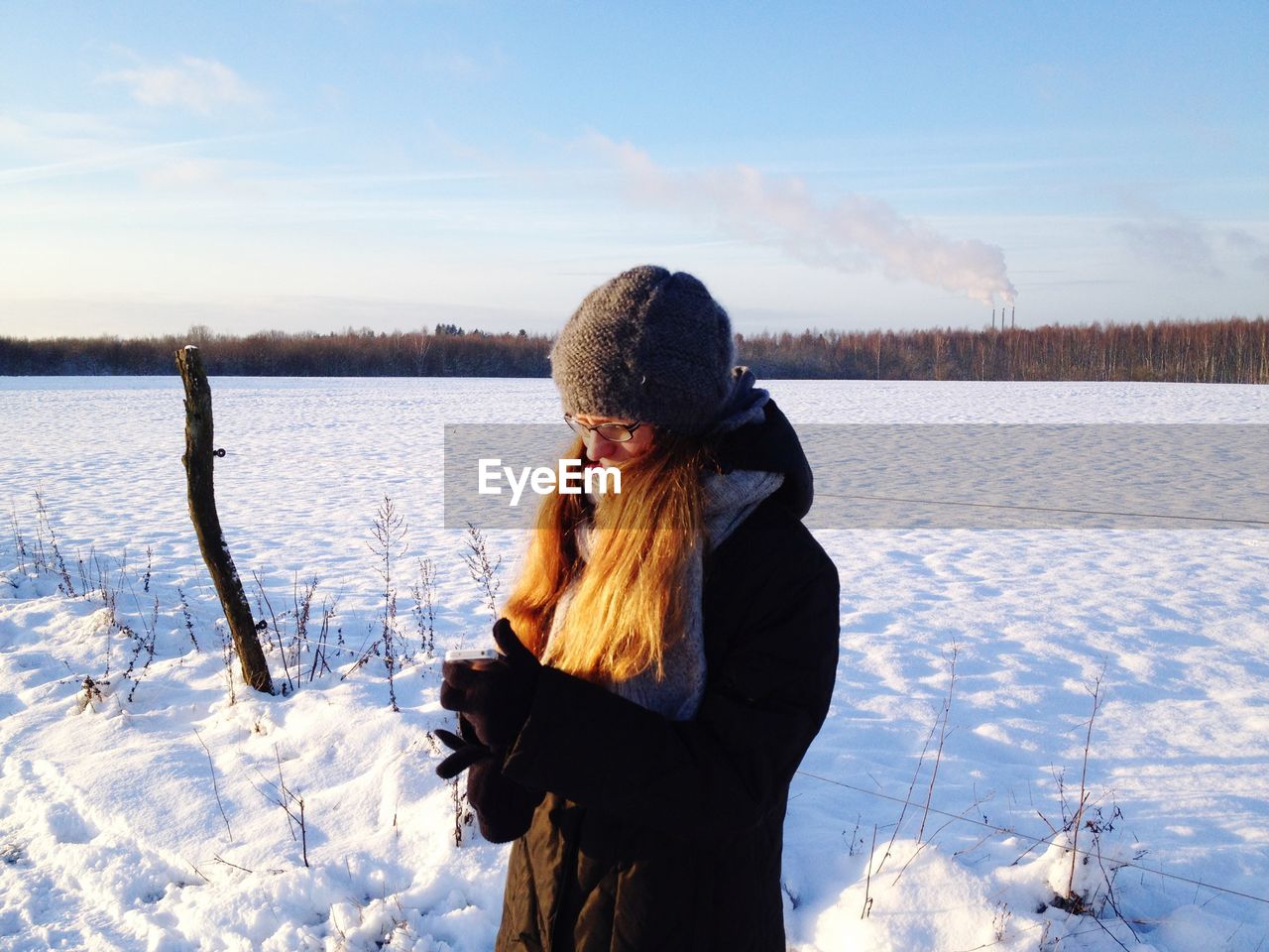 Woman using mobile phone while standing on snow against sky during winter