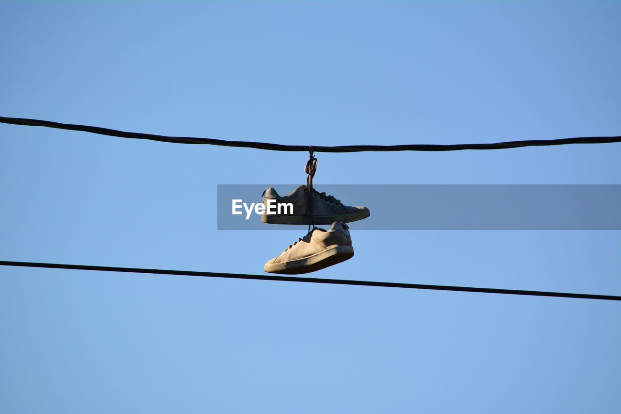 Low angle view of shoes hanging on cable against clear blue sky