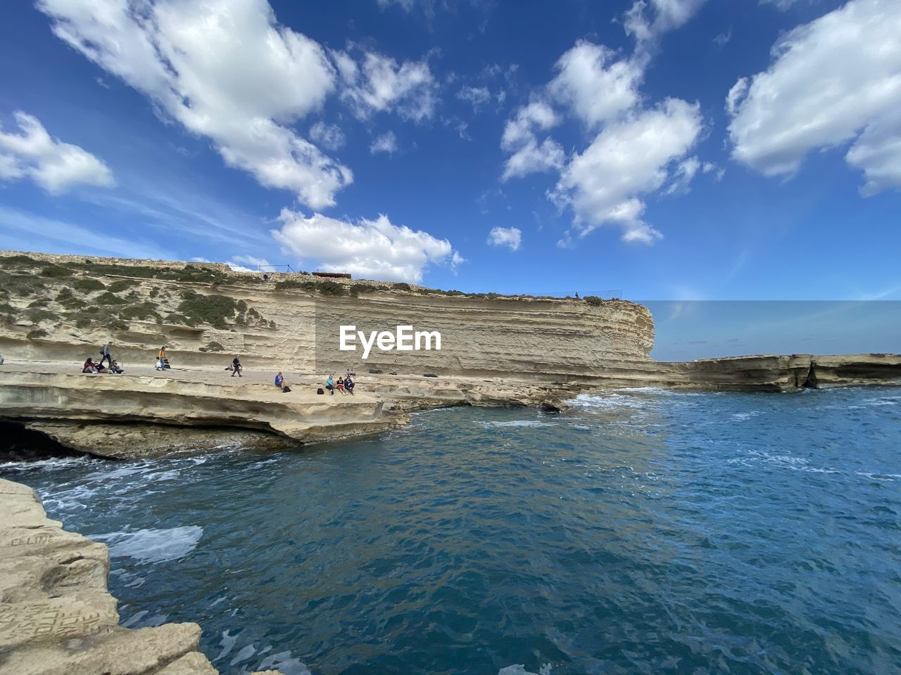 People sitting on rock formation by sea against sky