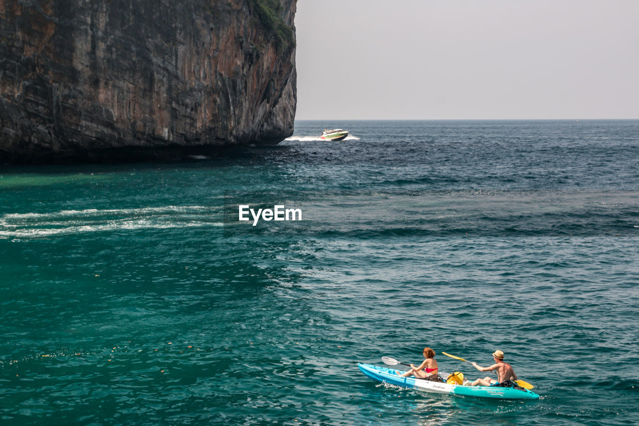 People kayaking on sea against sky