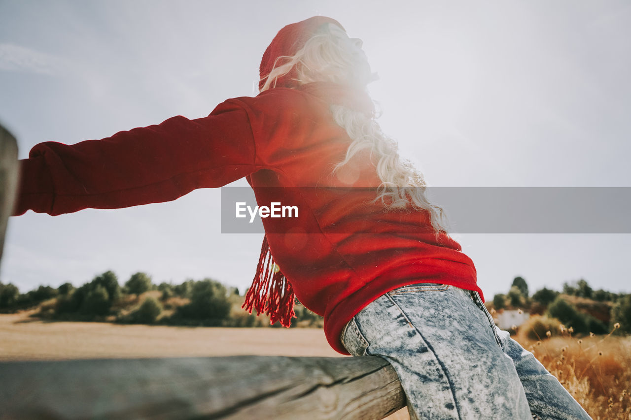 Side view of woman sitting on railing against clear sky during sunny day