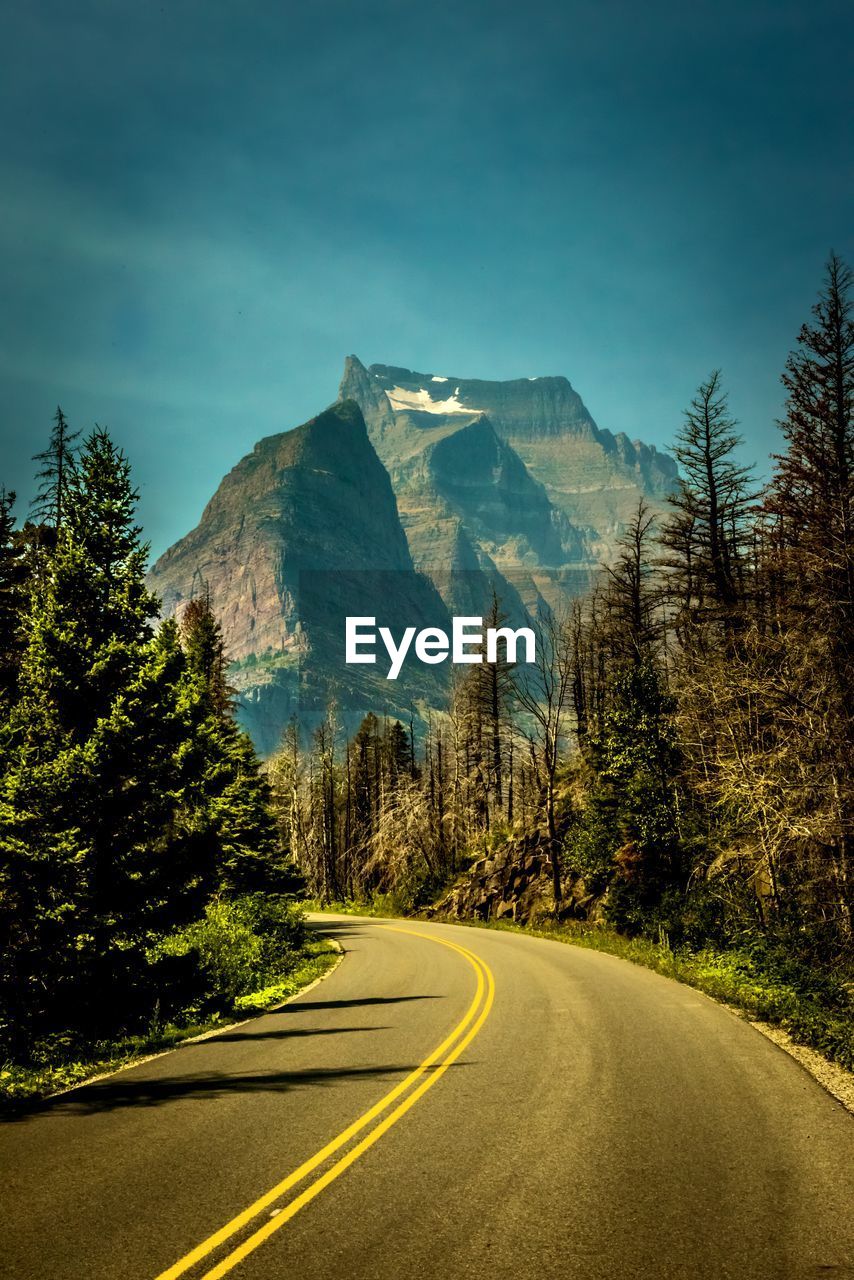 Road amidst trees and mountains against sky