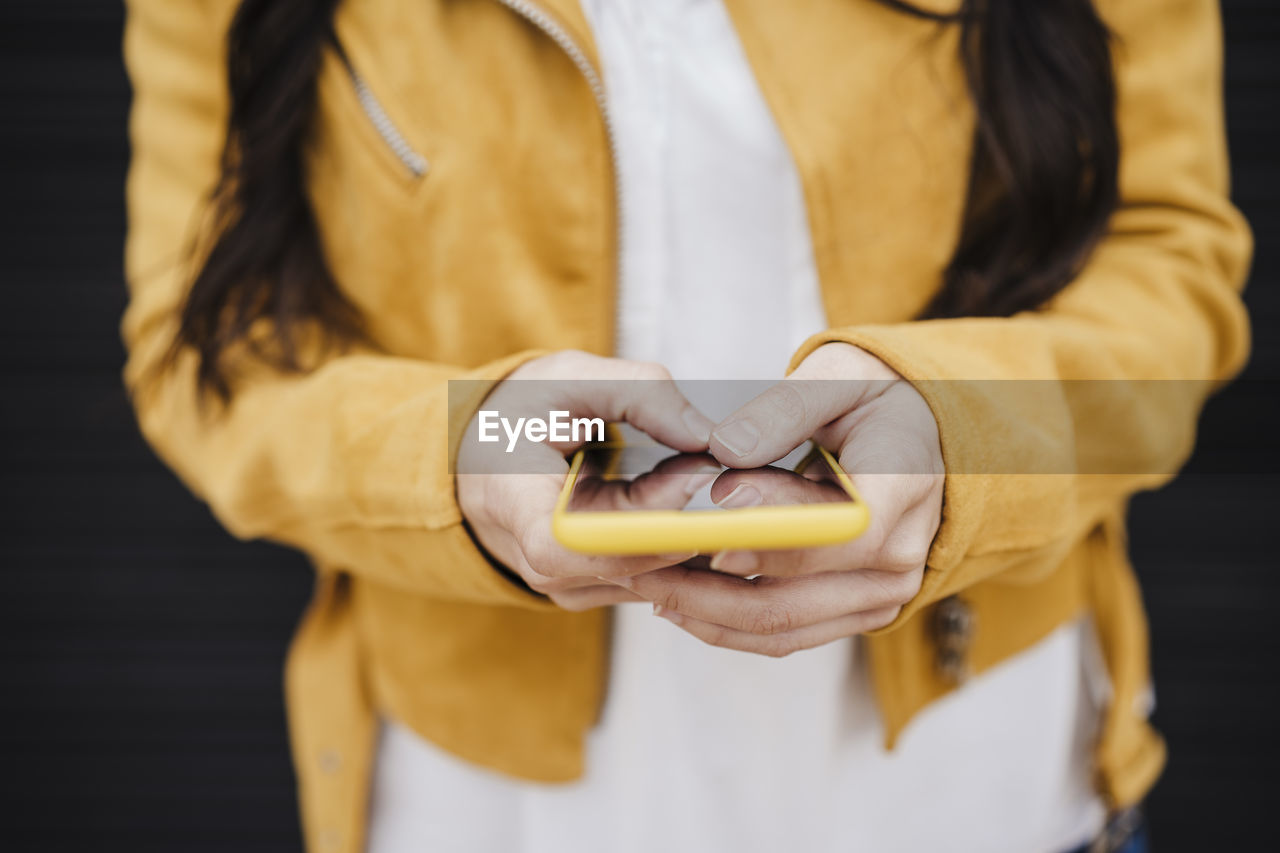 Mid adult woman in yellow jacket text messaging through smart phone