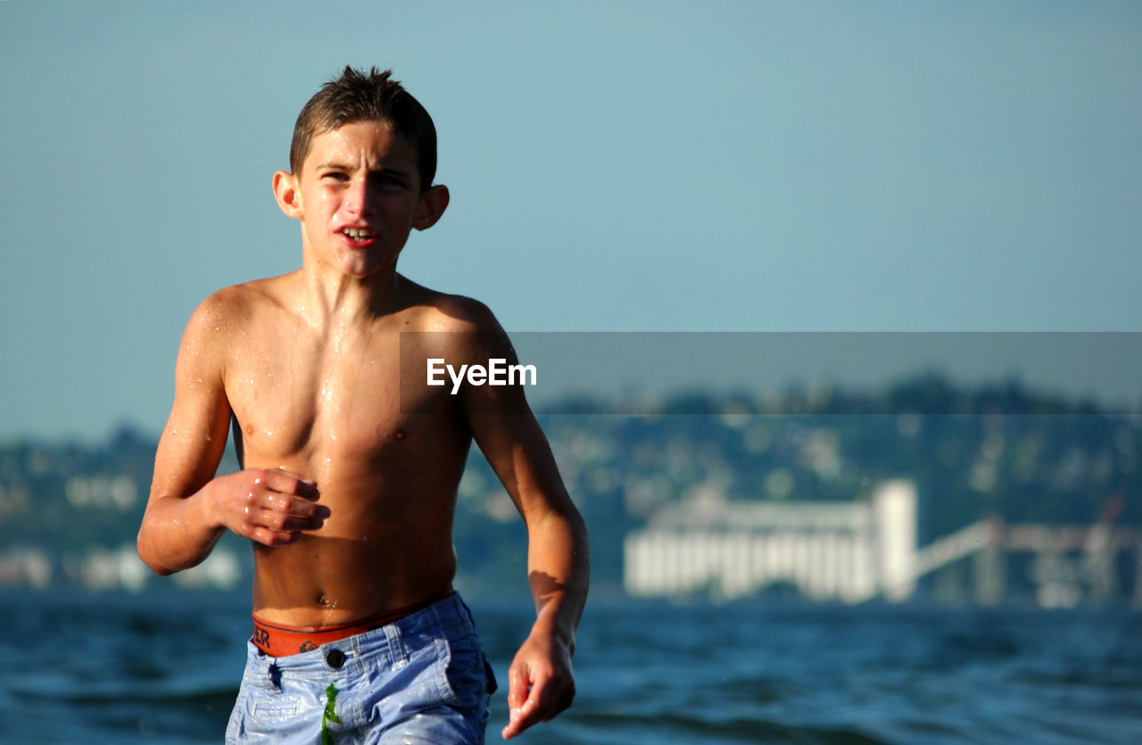 Portrait of shirtless boy walking in sea against sky