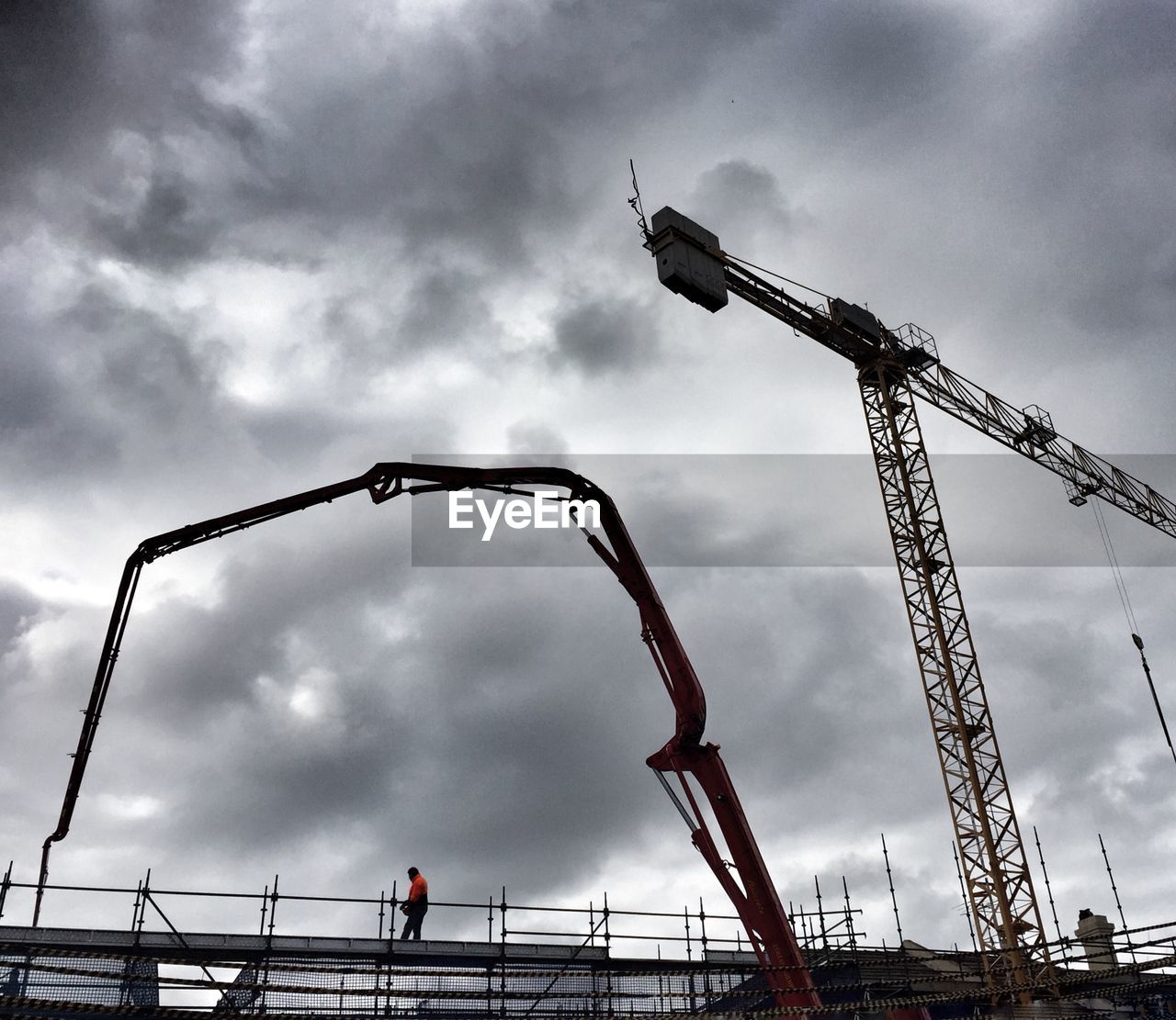 Low angle view of cranes and bridge against cloudy sky