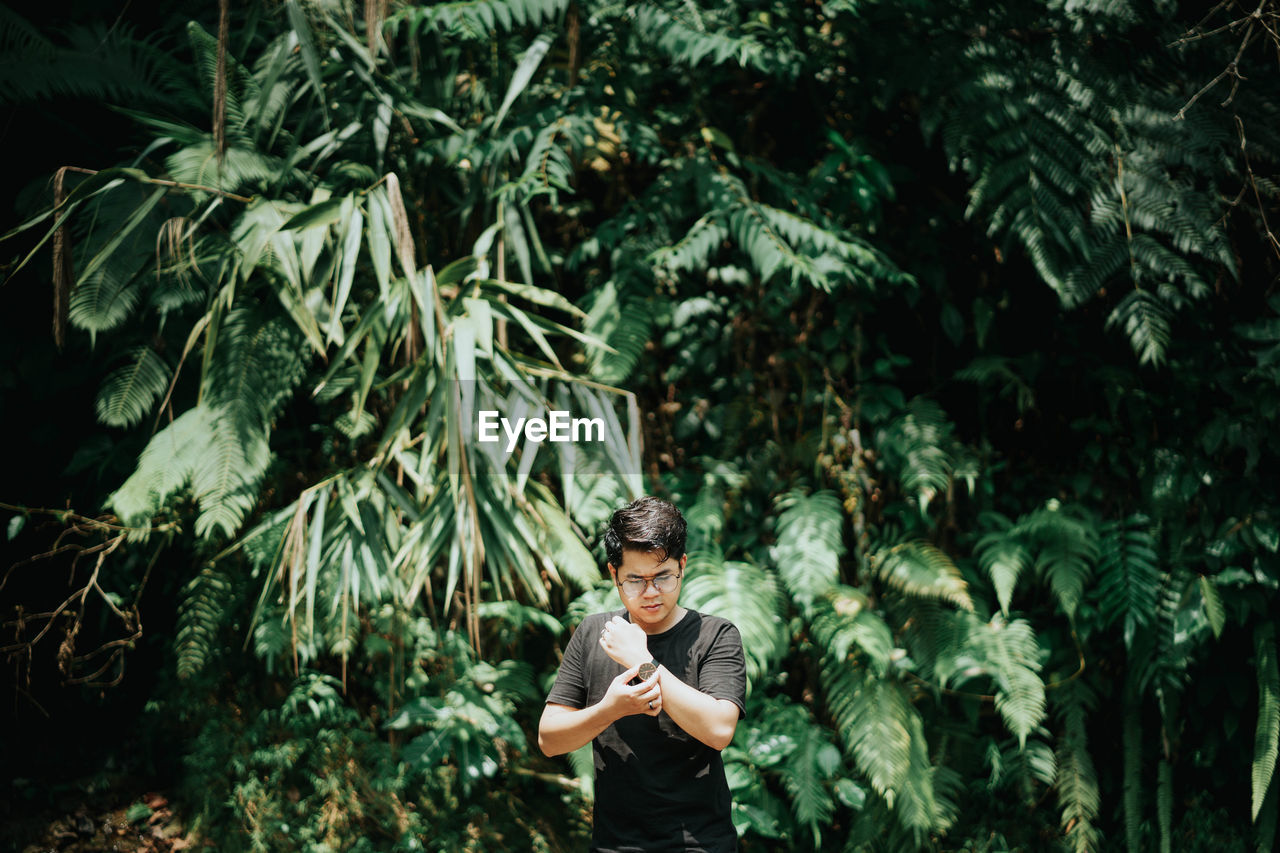 YOUNG MAN STANDING BY PLANTS