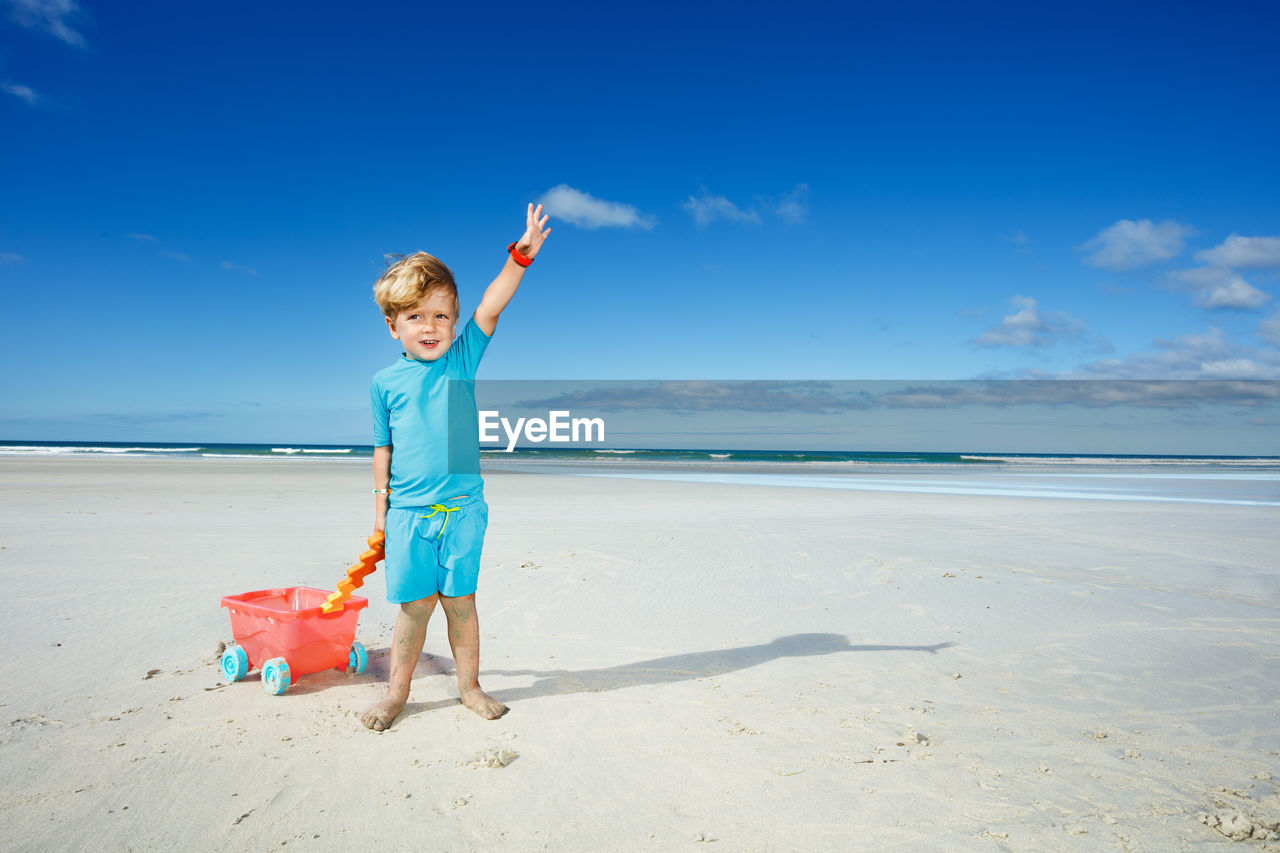 full length of boy playing with arms outstretched standing at beach
