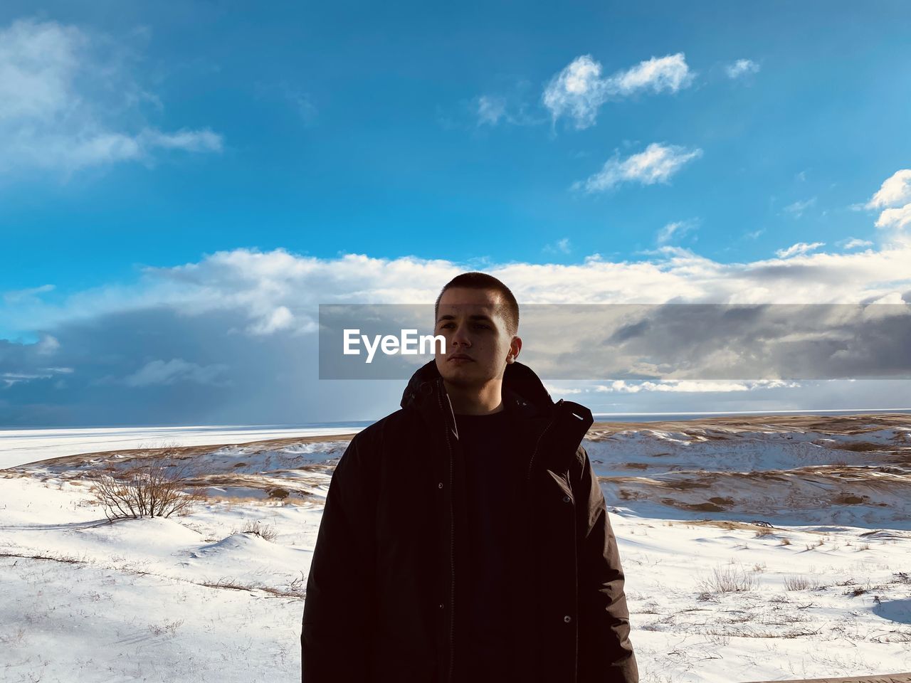 Young man standing on winter beach against sky