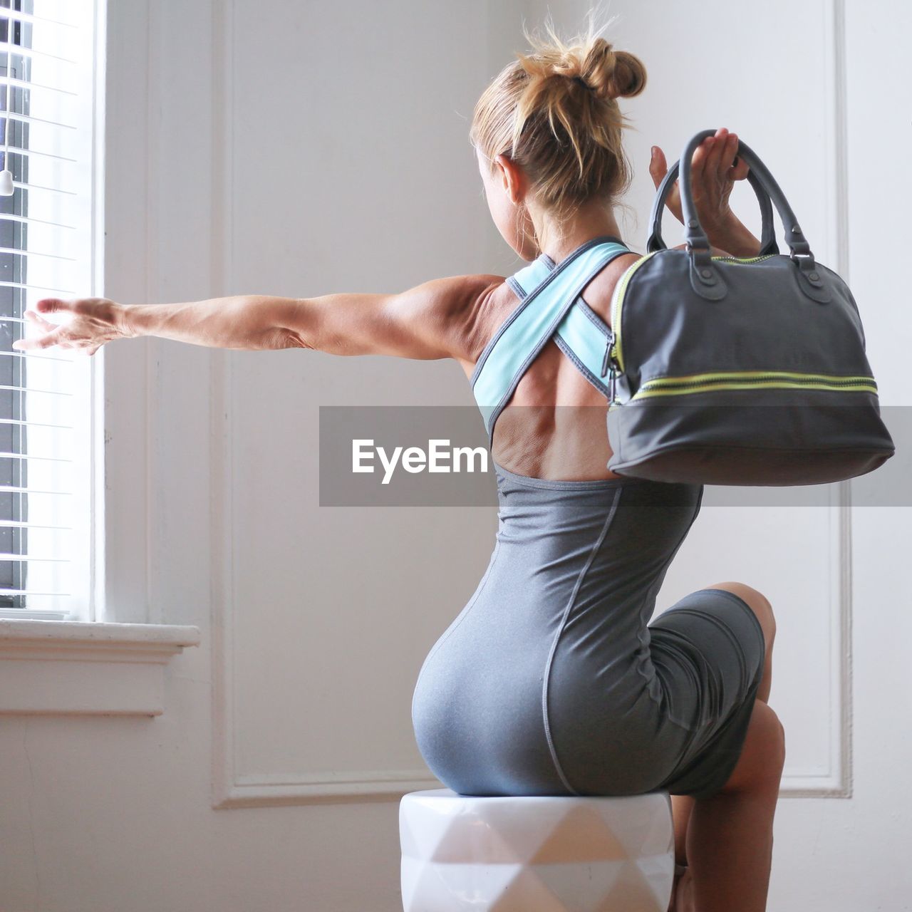 Rear view of athlete woman stretching while holding shoulder bag at home