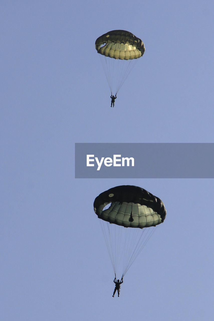 Low angle view of skydivers under parachutes against clear sky