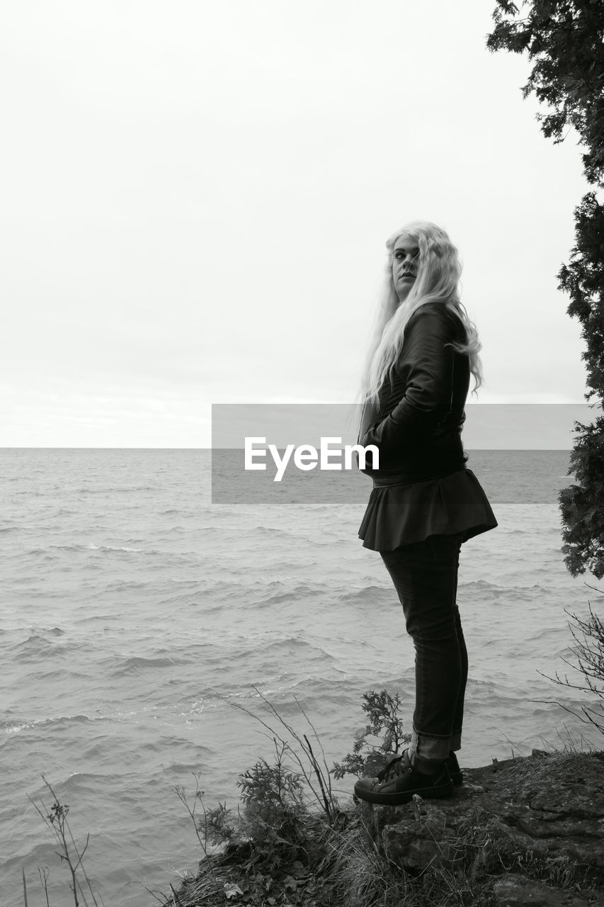 Side view of transgender male standing by sea against sky