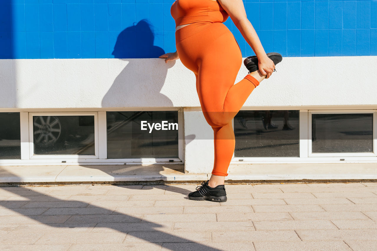 Side view of crop unrecognizable plump female athlete in sportswear exercising on tiled walkway in sunny town