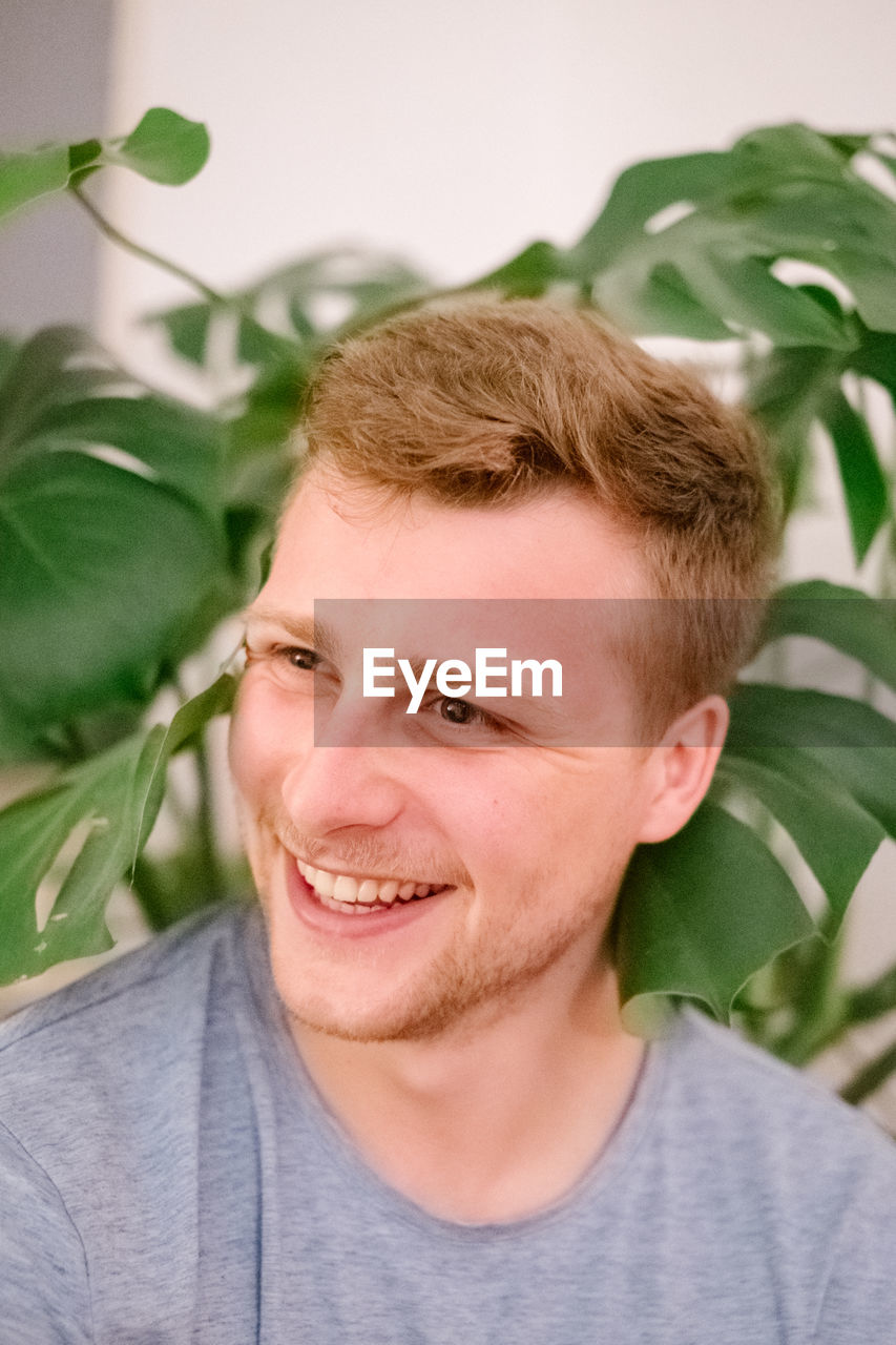 Close-up smiling of young man looking away while standing against plants