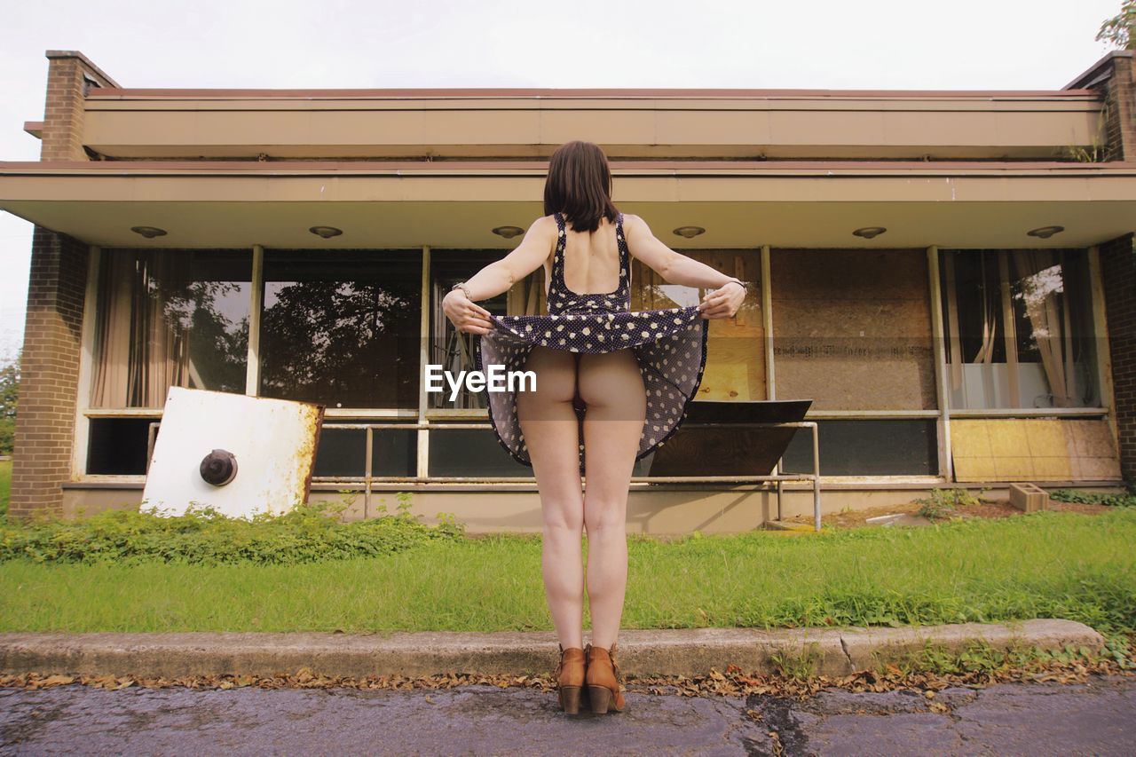 REAR VIEW OF WOMAN STANDING BY HOUSE
