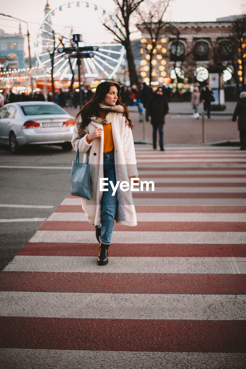 Teenage girl in warm clothing crossing road in city during winter