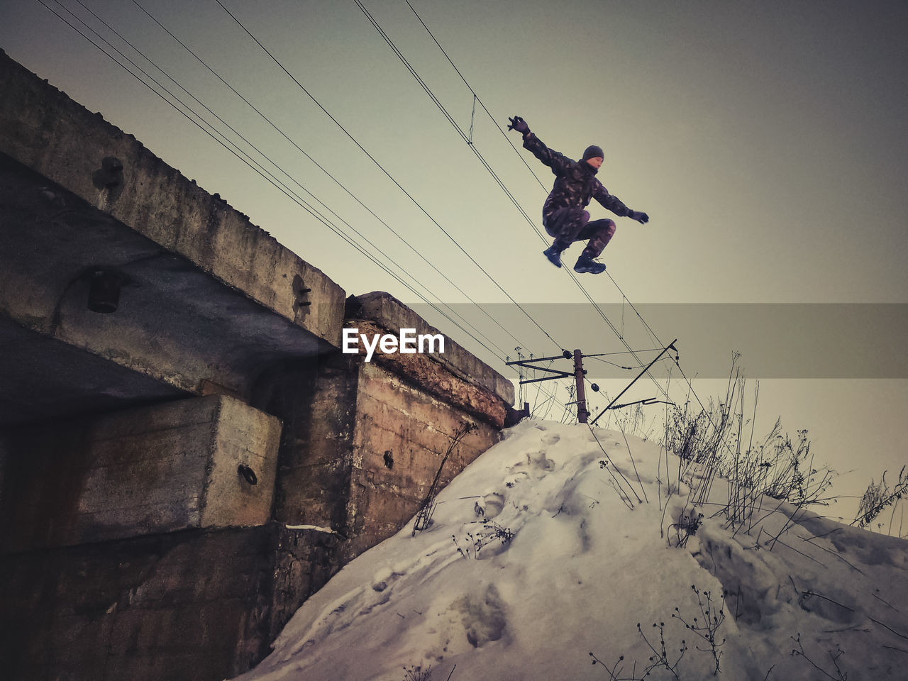 LOW ANGLE VIEW OF MAN JUMPING ON SNOW COVERED LANDSCAPE