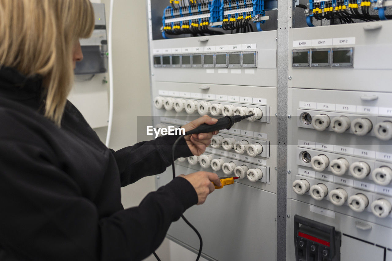 Female electrician with voltage tester repairing switchboard in meter room