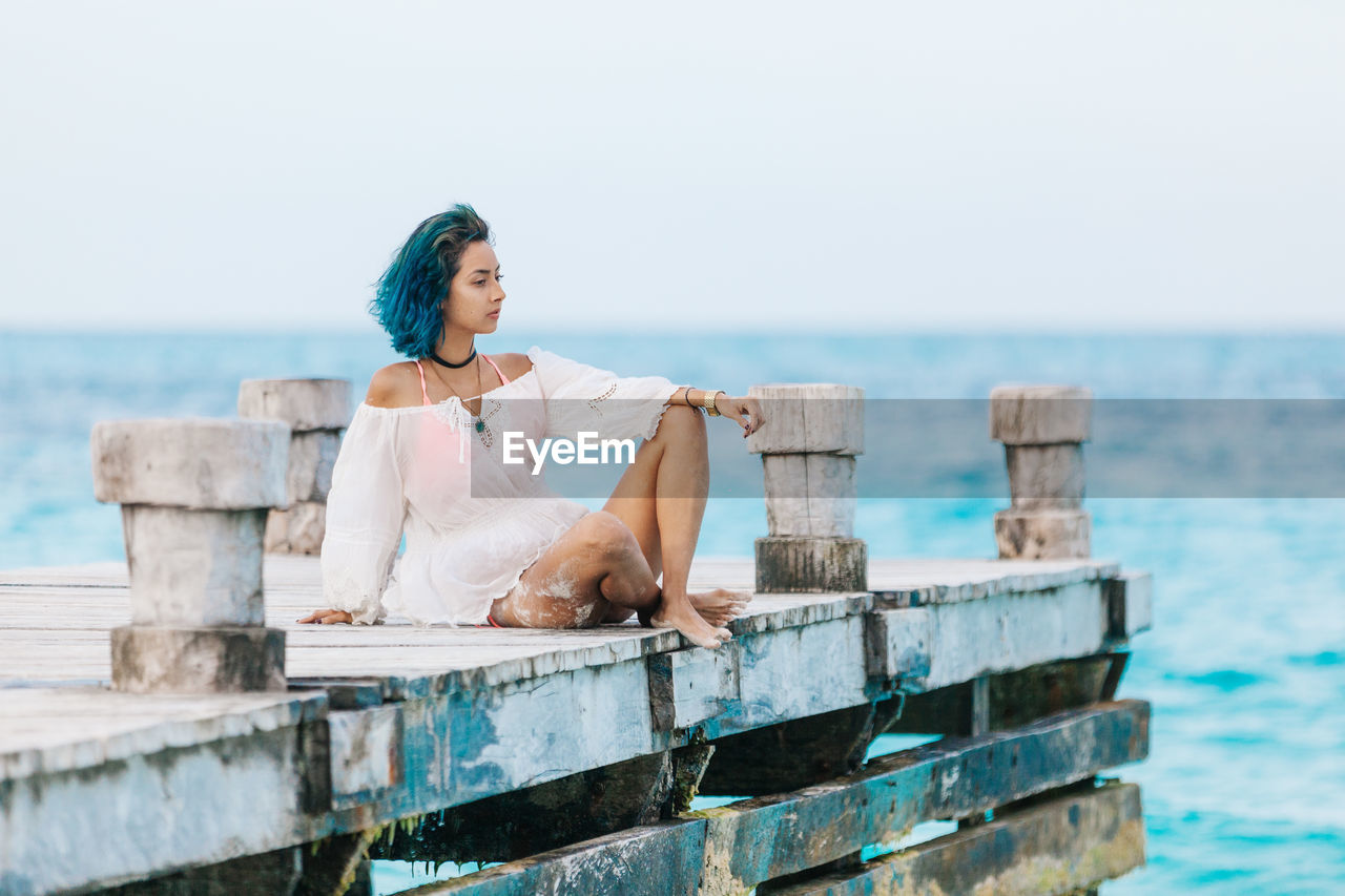 Full length of woman sitting on pier at beach against sky