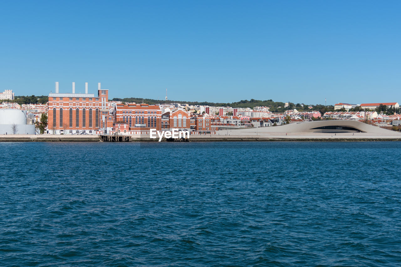 Sea by buildings against clear blue sky