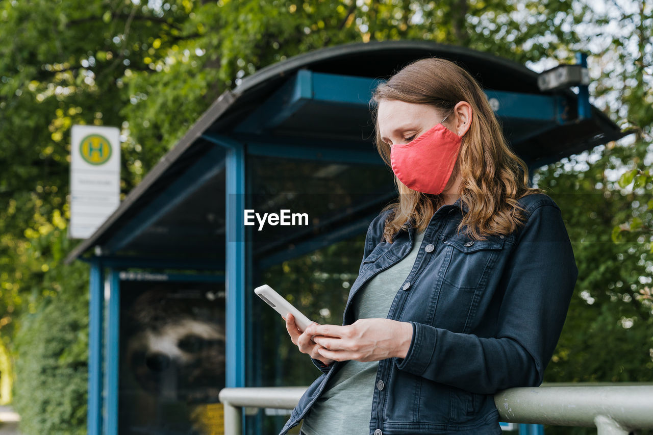 Woman wearing face mask using smart phone while standing by railing