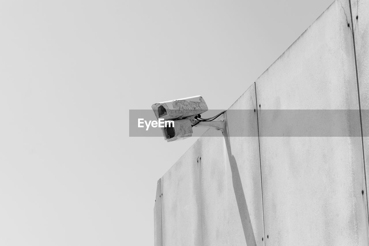 Low angle view of security camera on wall against sky