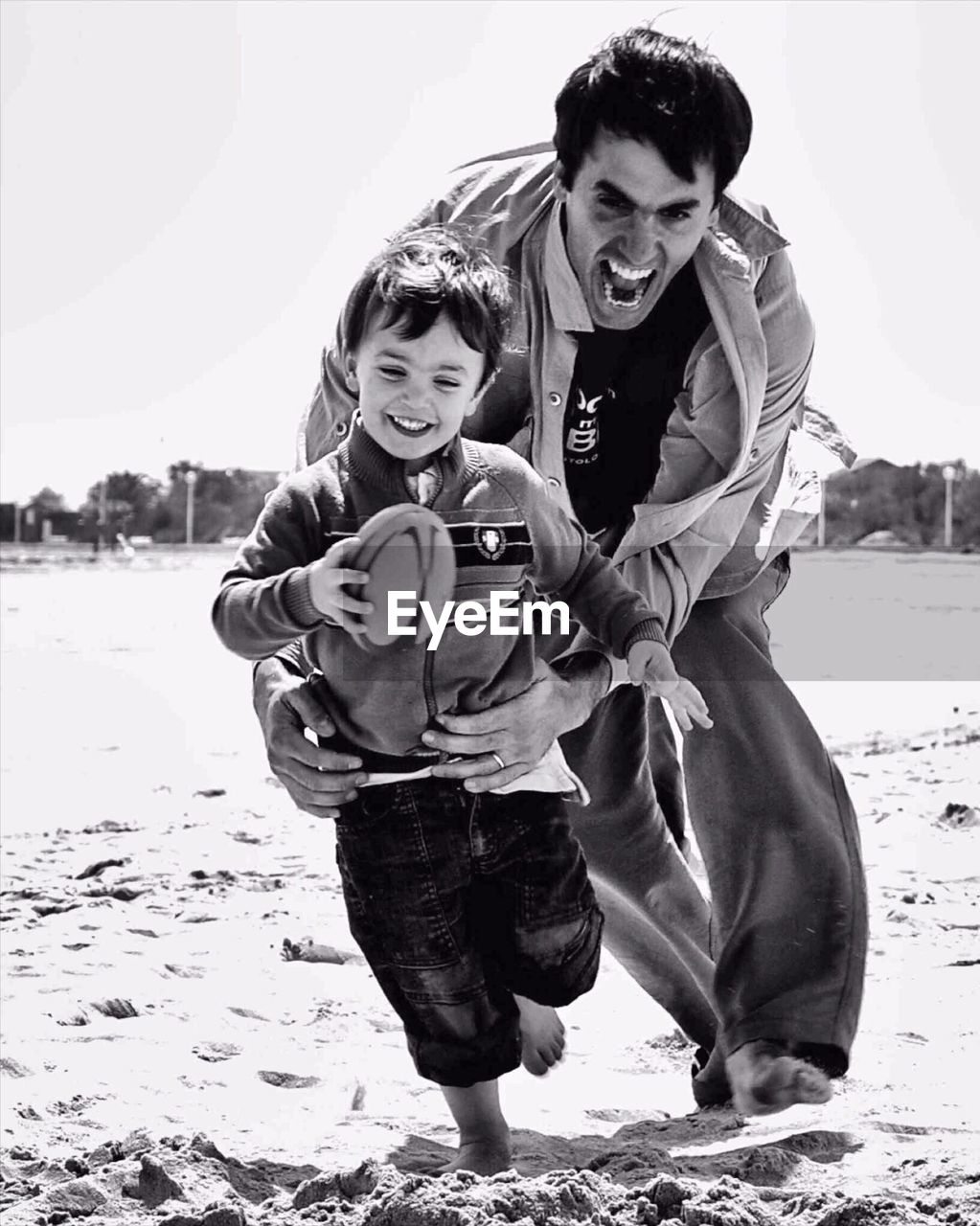 Father playing rugby game with son on beach